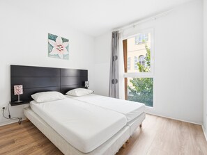 Ein Schlafzimmer mit einem Bett, Nachttischen, einer Lampe und einem Fenster mit Vorhängen.