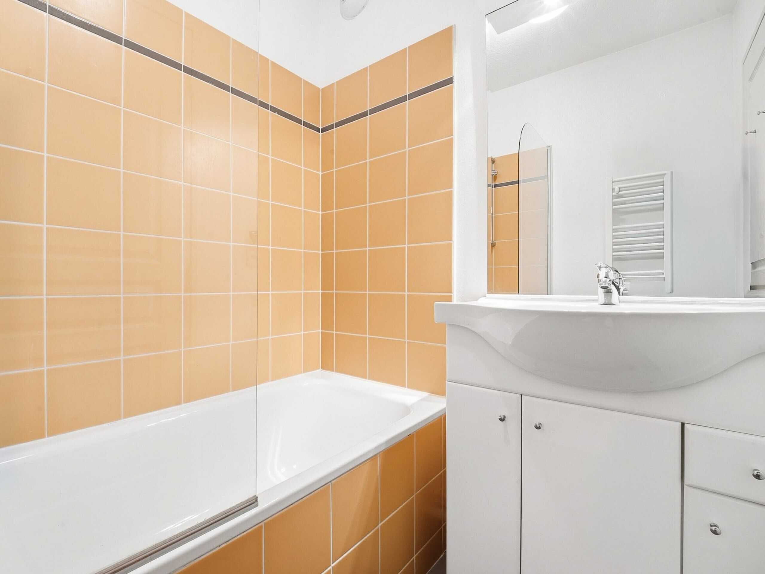 Une salle de bain avec une baignoire blanche, un lavabo blanc et des murs recouverts de carreaux orange.