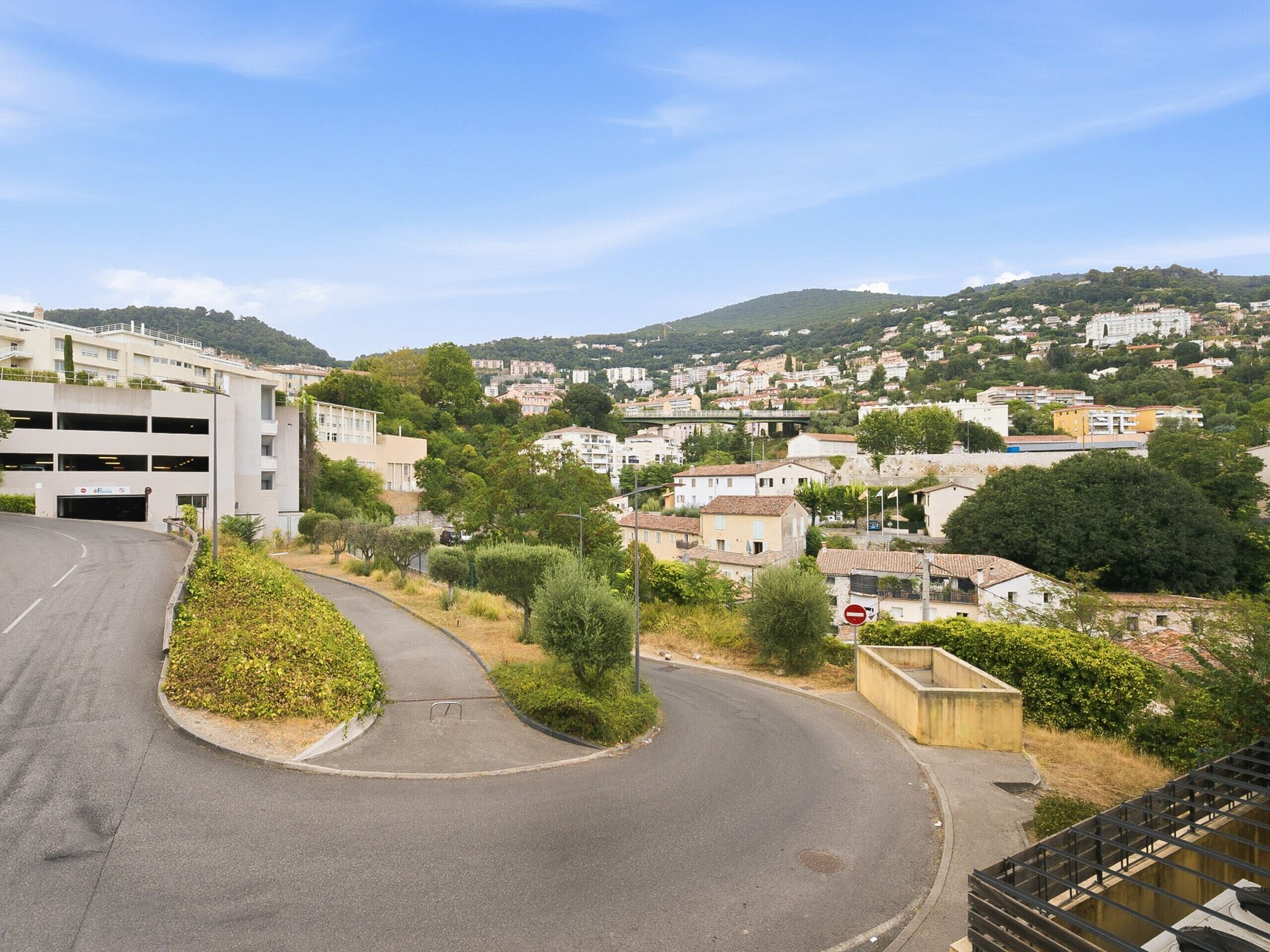 Ein Wohngebiet mit einer gewundenen Straße, einer Tiefgarage und Blick auf eine Hügelstadt.