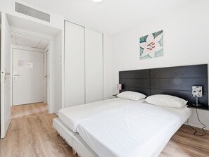 A bedroom with a bed, a nightstand, a wall-mounted lamp, and a door leading to another room. - Apartment with balcony and swimming pool (Grasse)