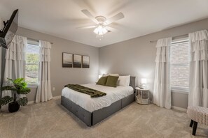 A bedroom with a bed, a ceiling fan, a nightstand, a lamp, and a potted plant. - Bentonville Belle • Bike Storage & Trails (Bentonville)