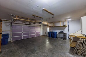 A garage with a purple garage door, a workbench, and two blue trash bins. - Bentonville Belle • Bike Storage & Trails (Bentonville)