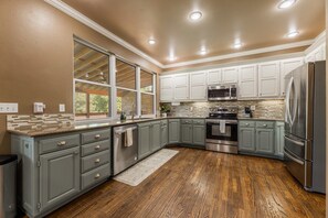 A modern kitchen with grey cabinets, stainless steel appliances, and a large window. - Bentonville Belle • Bike Storage & Trails (Bentonville)