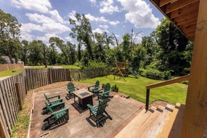 A patio with Adirondack chairs and a table, surrounded by a wooden fence and a grassy area with trees. - Double Black Diamond | Trails | Bike Out | 2 Decks (Bentonville)