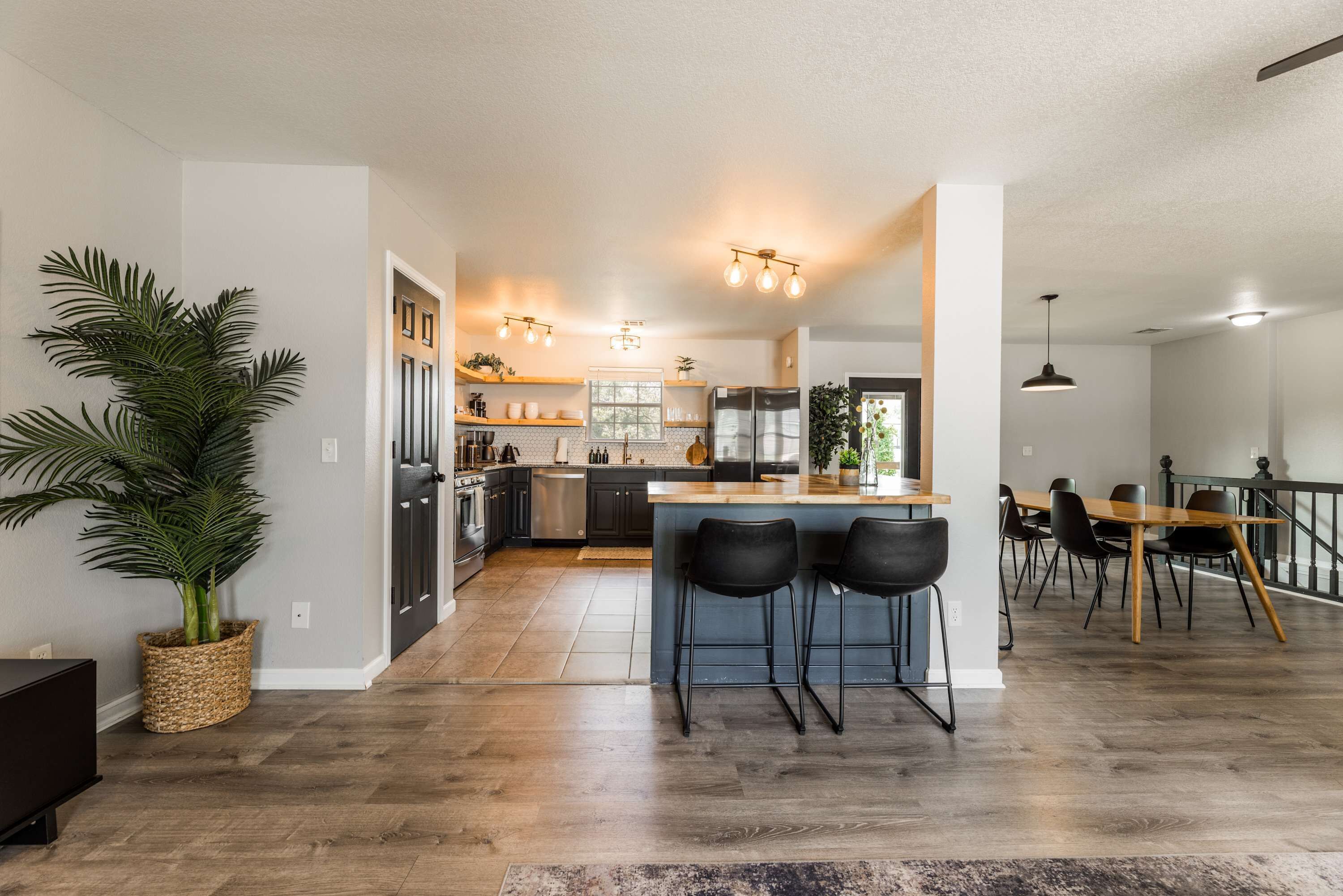 A modern kitchen with a central island, black bar stools, and a dining area with a wooden table and chairs.