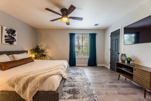 A bedroom with a bed, a ceiling fan, a window with curtains, a television, and a plant. - Double Black Diamond | Trails | Bike Out | 2 Decks (Bentonville)