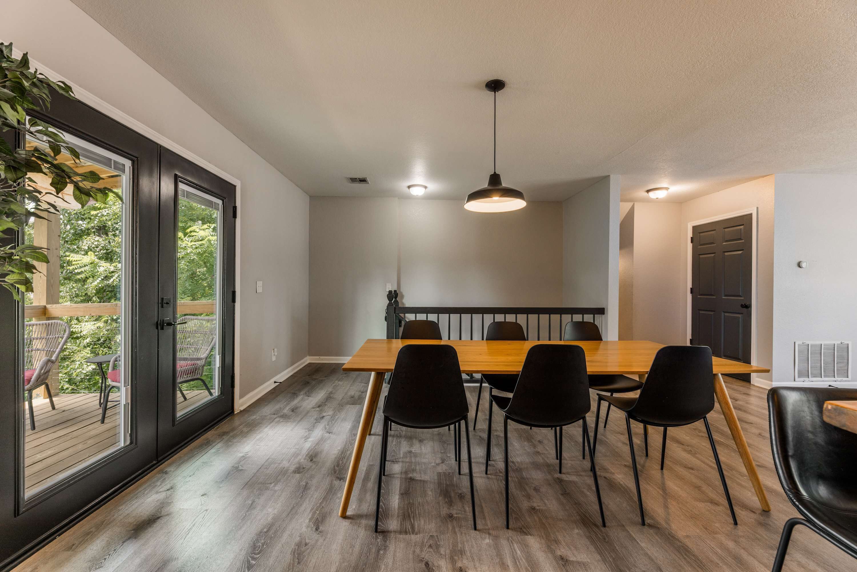A dining area with a wooden table and black chairs, a ceiling light, and a view through a glass door to an outdoor patio.
