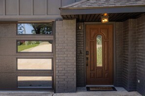 A residential entrance with a brown door, a garage door, and a small porch area. - Double Black Diamond | Trails | Bike Out | 2 Decks (Bentonville)