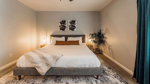 Ein Schlafzimmer mit Bett, Nachttischen, Deckenventilator, Wandbild und einer Topfpflanze.
