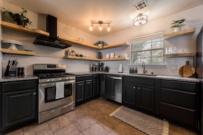 A modern kitchen with dark cabinetry, stainless steel appliances, and a hexagonal tile backsplash. - Double Black Diamond | Trails | Bike Out | 2 Decks (Bentonville)