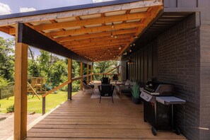 Um pátio coberto ao ar livre com deck de madeira, churrasqueira e mobiliário de exterior.