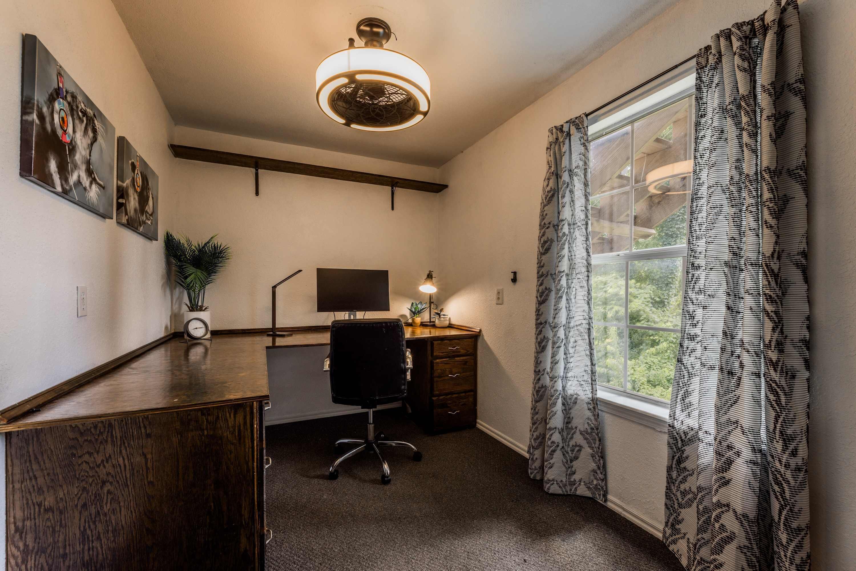 A room with a desk, chair, and a large window with patterned curtains.