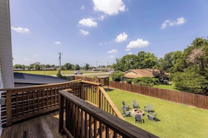 Une terrasse en bois avec un foyer et des chaises, donnant sur une cour arrière avec une pelouse et une clôture en bois.