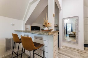 Eine Küche mit Barbereich, zwei Barhocker, einem großen Spiegel und Blick in das angrenzende Schlafzimmer.