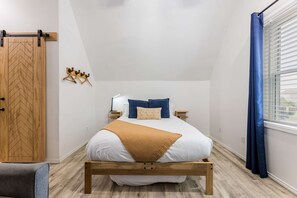 A bedroom with a bed, bedside tables, a lamp, a wardrobe, and a window with curtains. - The Loft | Modern Studio 5 Min to Downtown (Bentonville)