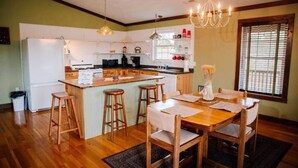 A kitchen with a central island, wooden bar stools, a dining table with chairs, and a chandelier.