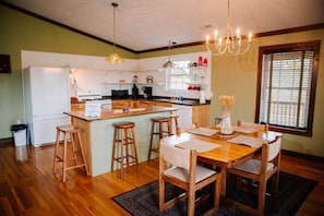 A kitchen with a central island, wooden bar stools, a dining table with chairs, and a chandelier.