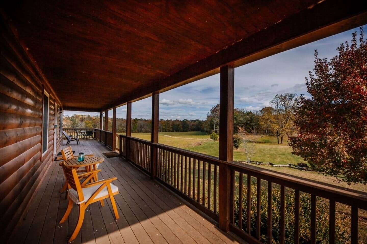 A wooden deck with a table and chairs, overlooking a grassy field and trees.