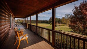A wooden deck with a table and chairs, overlooking a grassy field and trees.