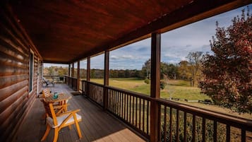 Une terrasse en bois avec une table et des chaises, donnant sur un champ verdoyant et des arbres.