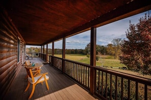 A wooden deck with a table and chairs, overlooking a grassy field and trees.