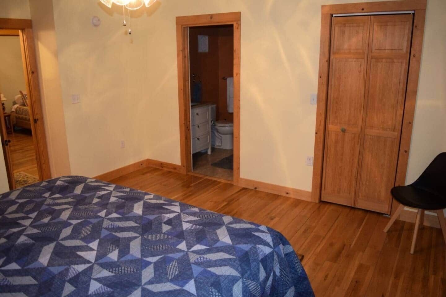 A bedroom with a bed, a wooden wardrobe, and a bathroom visible through an open door.