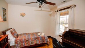 A bedroom with a bed, a desk, a chair, a ceiling fan, and a window with curtains.