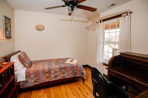 A bedroom with a bed, a desk, a chair, a ceiling fan, and a window with curtains.