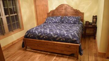 A wooden bed with a geometric patterned bedspread in a room with wooden flooring and a wooden door.