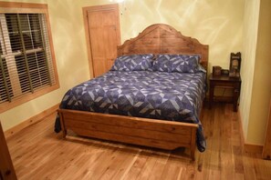A wooden bed with a geometric patterned bedspread in a room with wooden flooring and a wooden door. - Cripple Creek | New River Trail | Horses Allowed (Wythe County)