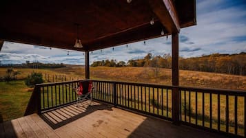 A wooden deck with a red chair, a hanging light fixture, and a view of a grassy field.
