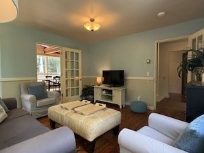 A living room with a sofa, ottoman, TV stand, and a door leading to another room.