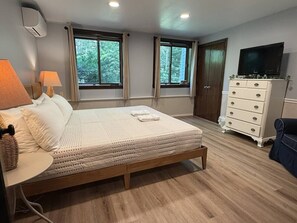 A bedroom with a bed, bedside lamps, a dresser, a television, and windows with curtains.