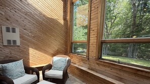 A wooden-paneled room with two wicker chairs and a small table, a window with a view of trees, and a wall-mounted air vent. - 5BR near Park & Downtown Bar Harbor! [North Lodge] (Bar Harbor)