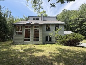 A two-story house with a front porch, a chimney, and a yard with grass and trees.