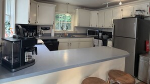 A modern kitchen with white cabinets, a built-in island, and a stainless steel refrigerator. - 5BR near Park & Downtown Bar Harbor! [North Lodge] (Bar Harbor)