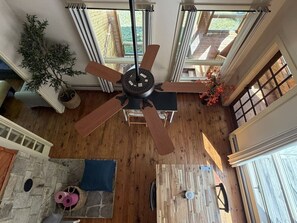 Un techo alto con un ventilador central, ventanas grandes y una pared de piedra.