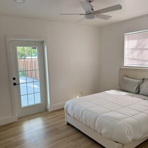 Une chambre à coucher comprenant un lit, un ventilateur de plafond, une fenêtre avec des stores et une porte donnant sur un espace extérieur.