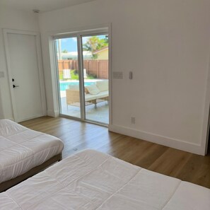 Une chambre avec deux lits, une porte-fenêtre coulissante donnant sur une terrasse et un plancher en bois.
