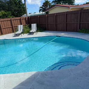 A swimming pool with a wooden fence, two striped lounge chairs, and a tiled deck. - Gorgeous 4-bedroom house with AC in lively Hollywood (Hollywood)