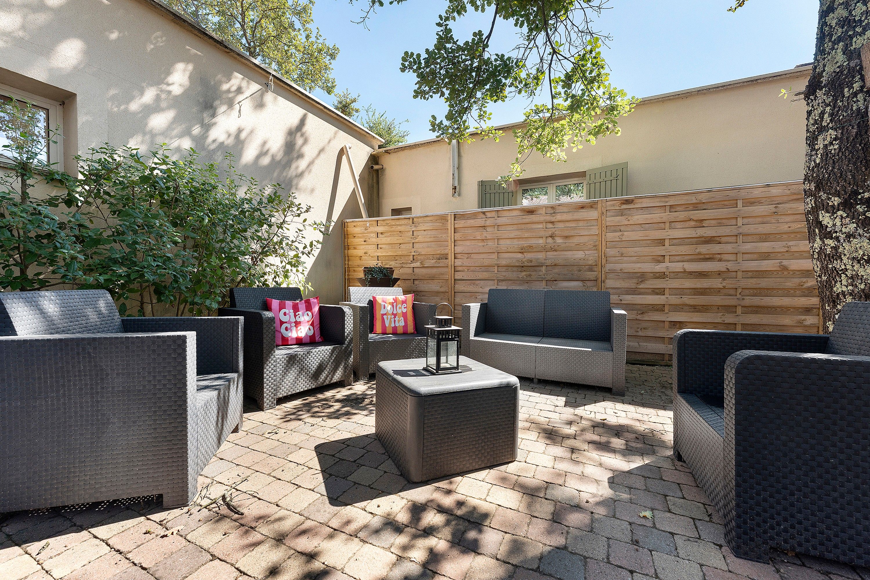 Un espace extérieur aménagé en terrasse, avec des meubles en osier, une clôture en bois et un sol en briques.