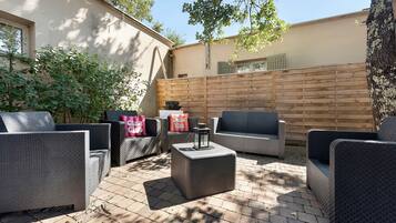Un espace extérieur aménagé en terrasse, avec des meubles en osier, une clôture en bois et un sol en briques.