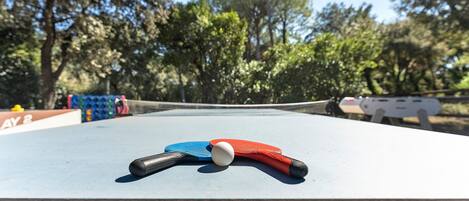 A table tennis table with a ball and rackets, surrounded by trees.
