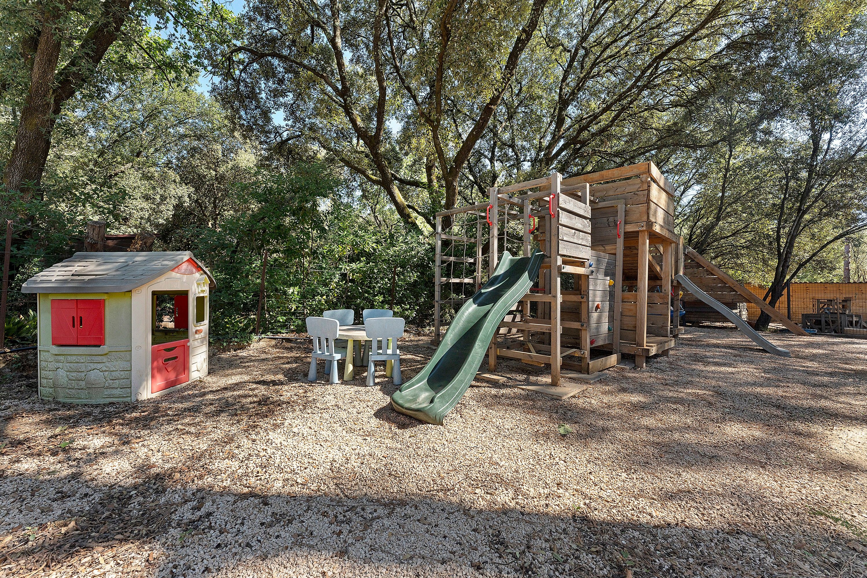 Ein Spielplatz mit Rutsche, Klettergerüsten und einem kleinen Gebäude mit roten Türen.