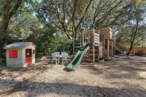 A playground with a slide, climbing structures, and a small building with red doors.