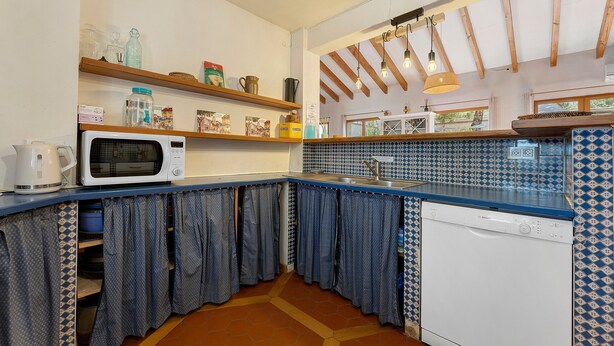 Cocina compacta con microondas, pileta y lavavajillas Bosch. Se observan estantes con distintos utensilios de cocina y un ventanal sobre la pileta.
