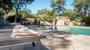 Un área junto a la piscina con sillones de descanso, una piscina y árboles circundantes.
