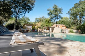 Un área junto a la piscina con sillones de descanso, una piscina y árboles circundantes.