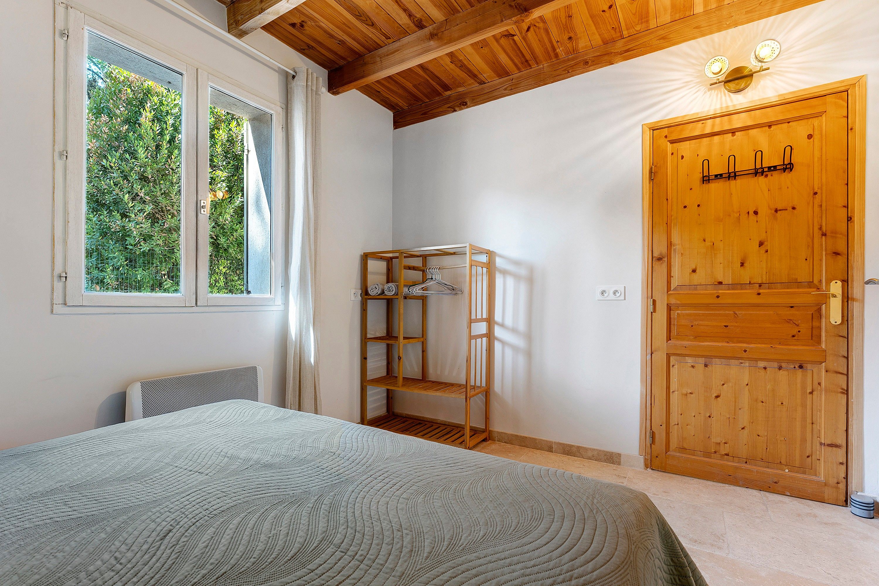 A bedroom with a bed, a wooden wardrobe, a window, and a door.