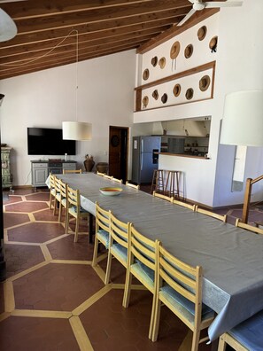 A spacious dining area with a long table, wooden chairs, a television, and a kitchen area with a refrigerator. - Mas Pepette Gîte for 24 with Pool, Hot Tub, River Access (Vers-Pont-du-Gard)